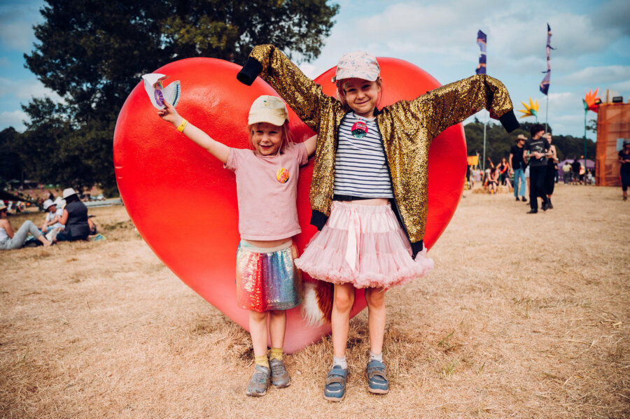 two young children standing in front of a big red heart at latitude festival
