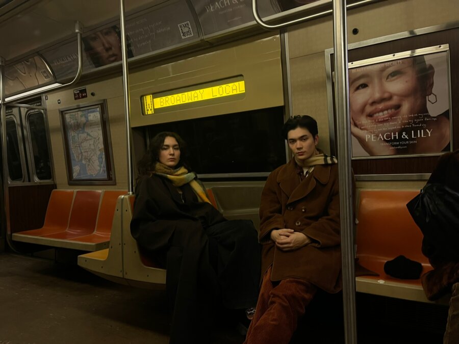Wasia Project (Olivia Hardy and Will Gao) sat on a Subway train wearing coats and scarves