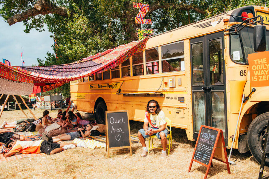 image of people sleeping outside of the Mind Body & Zen yellow school bus at Latitude, with a blackboard sign that says 'quiet area'.
