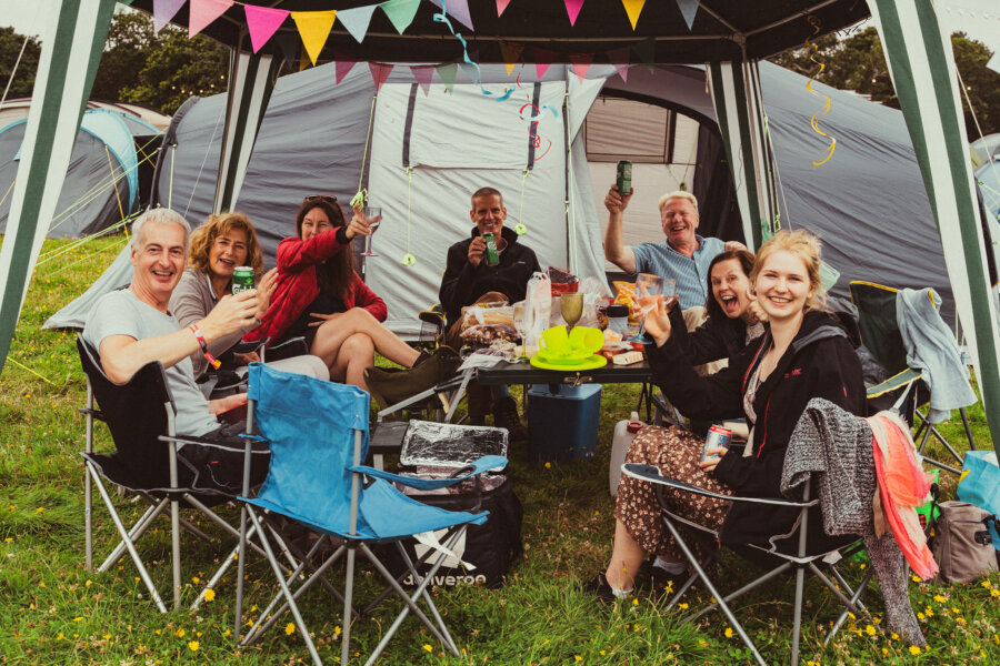 a family sat under a gazebo in the campsite, smiling at the camera